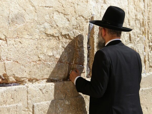 man in black long sleeve shirt and brown cowboy hat standing beside brown concrete wall during