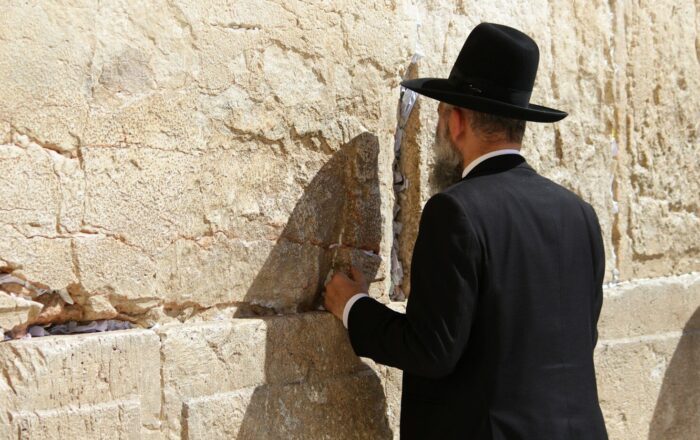 man in black long sleeve shirt and brown cowboy hat standing beside brown concrete wall during
